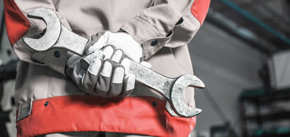 factory worker holding large wrench behind back in factory wearing protective clothing and gloves